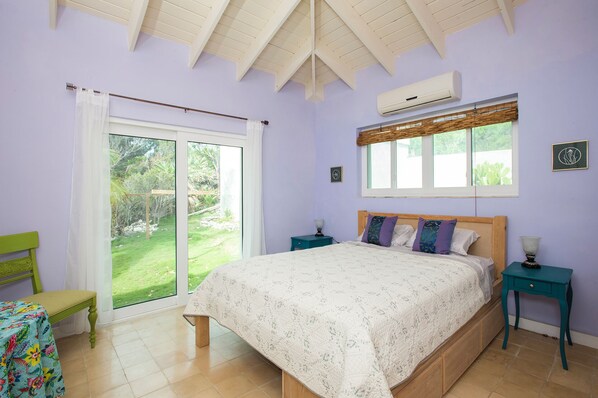 A bedroom with a bed, a window, a door, and a small table. - Island Paradise: Secluded Beachfront Retreat With Pool (Rainbow Bay)