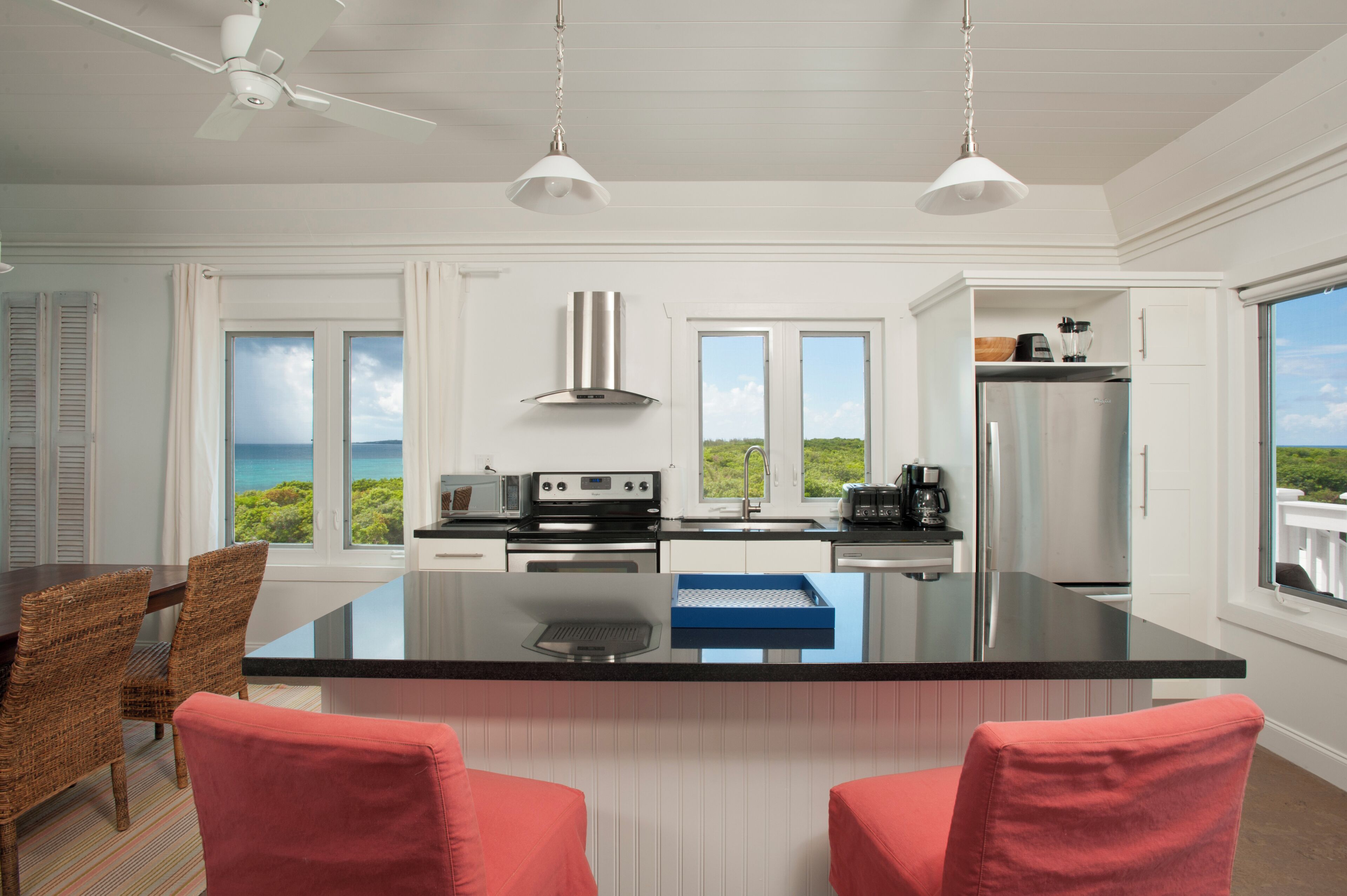 Een moderne keuken met een groot eiland, witte kasten en uitzicht op zee.