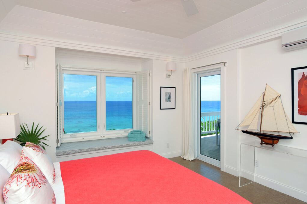 Ein Schlafzimmer mit einem großen Bett, Blick auf den Ozean, einem Modell eines Segelbootes und einem Balkon.