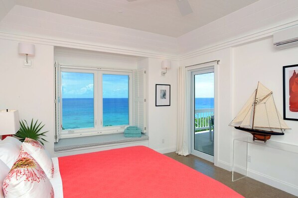 A bedroom with a large bed, a view of the ocean, a sailboat model, and a balcony. - Oceanfront Hideaway: Luxurious Retreat With Stunning Views (Governor's Harbour)