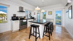 A modern kitchen with a central island, stainless steel appliances, and a view to the outdoors. - Island Hideout: Quaint Cottage, Moments From The Beach (James Cistern)