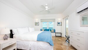 A bedroom with a bed, nightstand, dresser, and a view of the ocean. - Island Hideout: Quaint Cottage, Moments From The Beach (James Cistern)