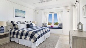 Een slaapkamer met een bed, nachtkastjes, een raam met gordijnen, een plafondventilator en uitzicht op het omliggende landschap.