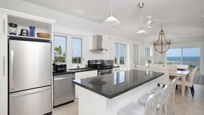 Een moderne keuken met een groot eiland, roestvrijstalen apparatuur en uitzicht op zee.
