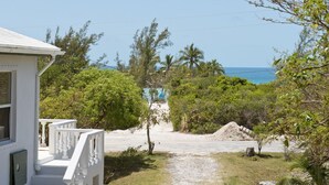 Ein weißes Gebäude mit Balkon, ein Kiesweg, der zum Strand führt, und dichtes Grün.