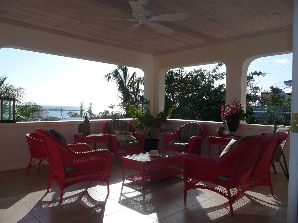 A covered outdoor seating area with red wicker furniture, a ceiling fan, and a view of the ocean.