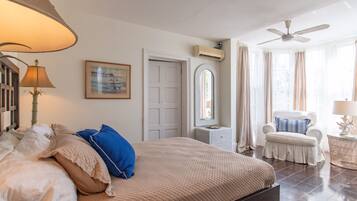 A bedroom with a bed, a chair, a lamp, a ceiling fan, and a window with curtains.
