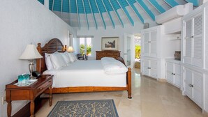 A bedroom with a large bed, wooden headboard, bedside tables, a nightstand, a lamp, a framed picture, a window, and a view of the outside. - Exquisite Retreat: Contemporary Estate On Pink Sand Beach (Double Bay)