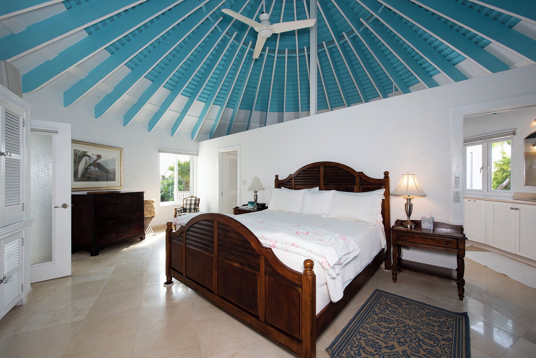 Ein Schlafzimmer mit einem großen Bett, einer Holzkommode, einem Schreibtisch mit Lampe und einer Decke mit blauen Balken.