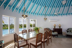 A dining area with a large table, chairs, and a view of the ocean through large windows. - Exquisite Retreat: Contemporary Estate On Pink Sand Beach (Double Bay)