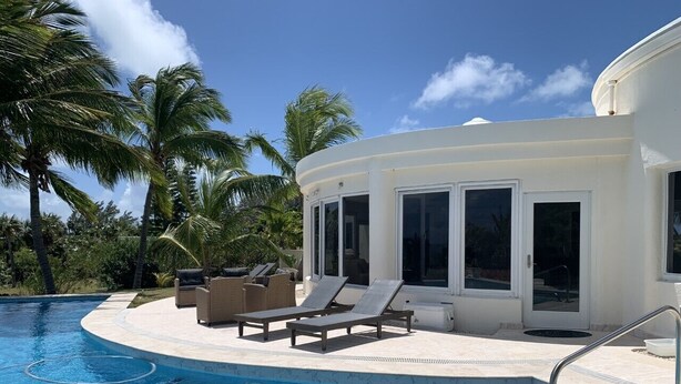 A pool area with lounge chairs and a building with large windows. - Exquisite Retreat: Contemporary Estate On Pink Sand Beach (Double Bay)