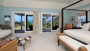 Un dormitorio con una cama grande, un sofá, una silla y vista al océano a través de puertas correderas de vidrio.