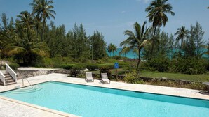 Une piscine rectangulaire bordée d’une terrasse en pierre, avec deux chaises longues et un escalier menant à un espace abrité.