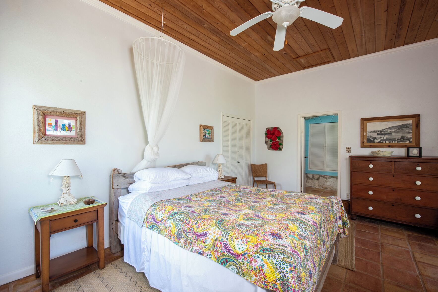 A bedroom with a bed, a wooden nightstand, a dresser, a ceiling fan, and a door with a blue frame.