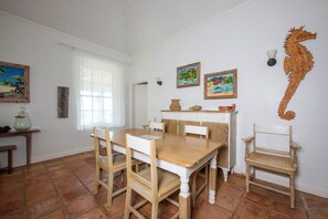A dining area with a wooden table and chairs, a seahorse wall decoration, and two framed paintings. - Sunset Splendor: Historic Beach House With Pool (Governor's Harbour)