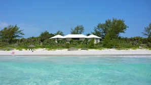 A beachfront property with a white building, clear turquoise water, and a sandy beach. - Oceanfront Elegance: Lovely Home With Views (Savannah Sound)
