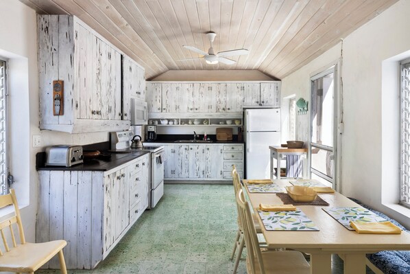 A kitchen with wooden cabinets, a dining table with chairs, and a ceiling fan. - Captain'S Cove: Historic House Near Town And Beach (Governor's Harbour)