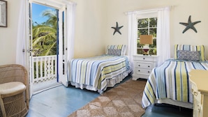 A bedroom with two beds, a wicker chair, a view of palm trees, and starfish decorations. - Captain'S Cove: Historic House Near Town And Beach (Governor's Harbour)
