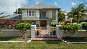 A two-story house with a front porch, a gated entrance, and a well-maintained garden with tropical plants.