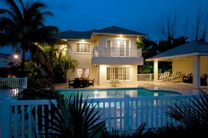 A two-story house with a swimming pool, white picket fence, and outdoor furniture.