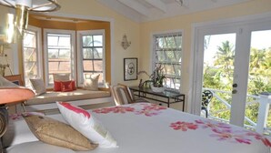 A bedroom with a bed, a window seat, a table, and a view of the outdoors.