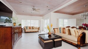 A spacious living room with a wooden ceiling, a sofa set, a coffee table, and a TV mounted on the wall.