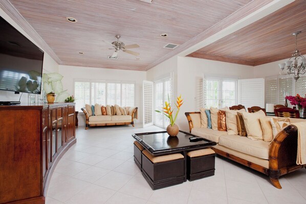 A spacious living room with a wooden ceiling, a sofa set, a coffee table, and a TV mounted on the wall.