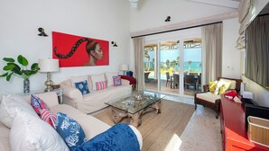 A spacious living room with a large glass door leading to a pool area, a ceiling fan, and a red artwork on the wall. - Wild Orchid Hideaway: Lux Beachfront Sanctuary (Governor's Harbour)