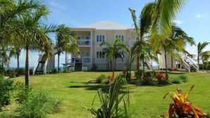 A multi-story hotel with a flat roof, surrounded by palm trees and a well-maintained lawn. - Coastal Haven: Charming Beachfront Cottage With Pool (Governor's Harbour)
