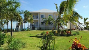 A multi-story hotel with a white exterior, surrounded by palm trees and a well-maintained lawn. - Oceanfront Bliss: Newly Built Luxury Home With Sunset Views (North Palmetto Point)