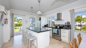 A modern kitchen with a central island, stainless steel appliances, and a view of the outdoors. - Oceanfront Bliss: Newly Built Luxury Home With Sunset Views (North Palmetto Point)