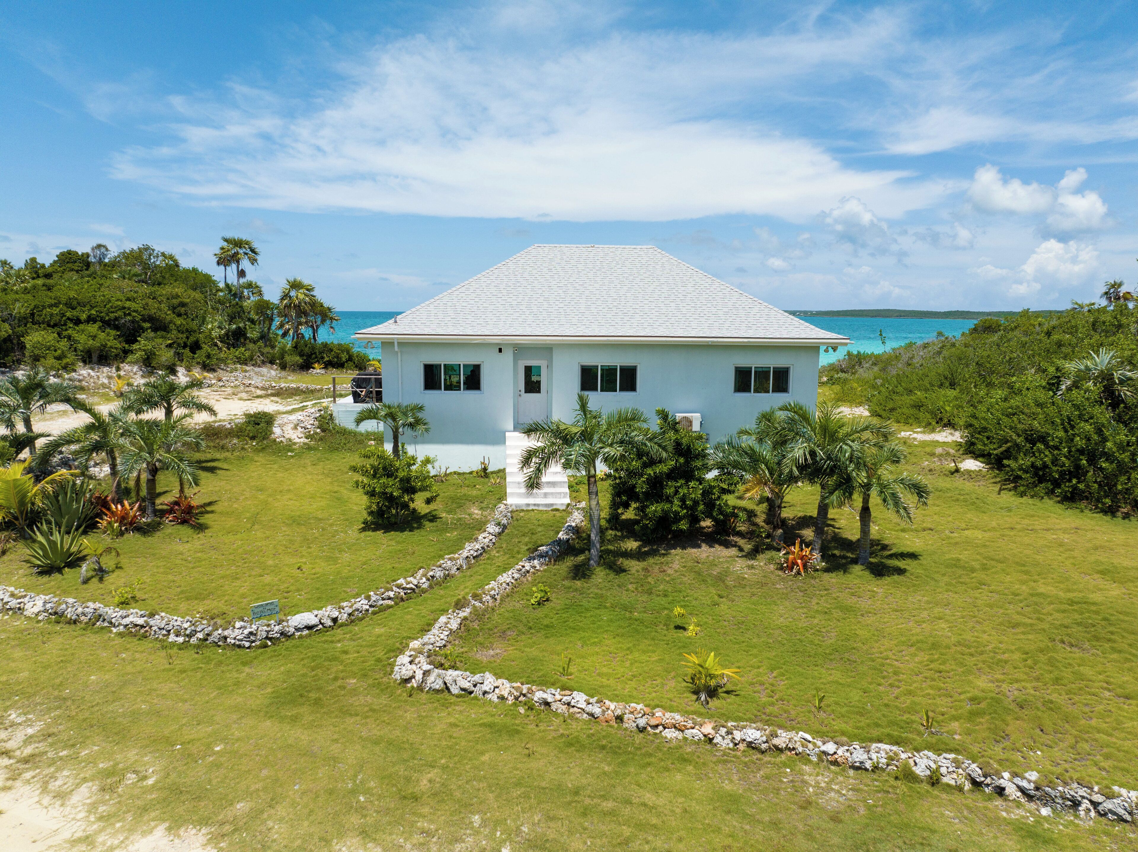 A white two-story house with a stone pathway leading to the entrance, surrounded by lush greenery and a view of the ocean.