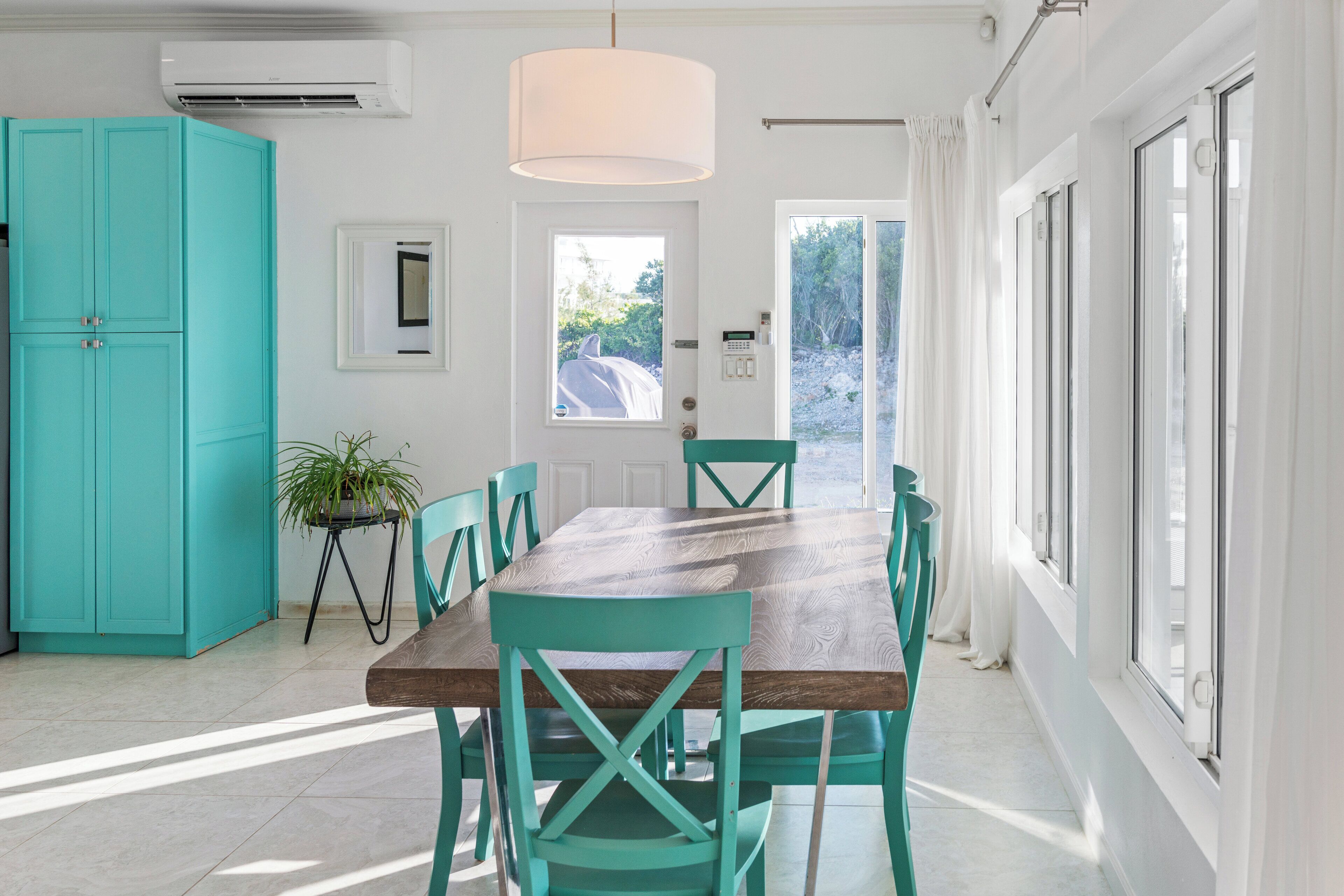 Un coin repas avec une table en bois et des chaises de couleur turquoise, une plante en pot et un meuble de rangement turquoise.