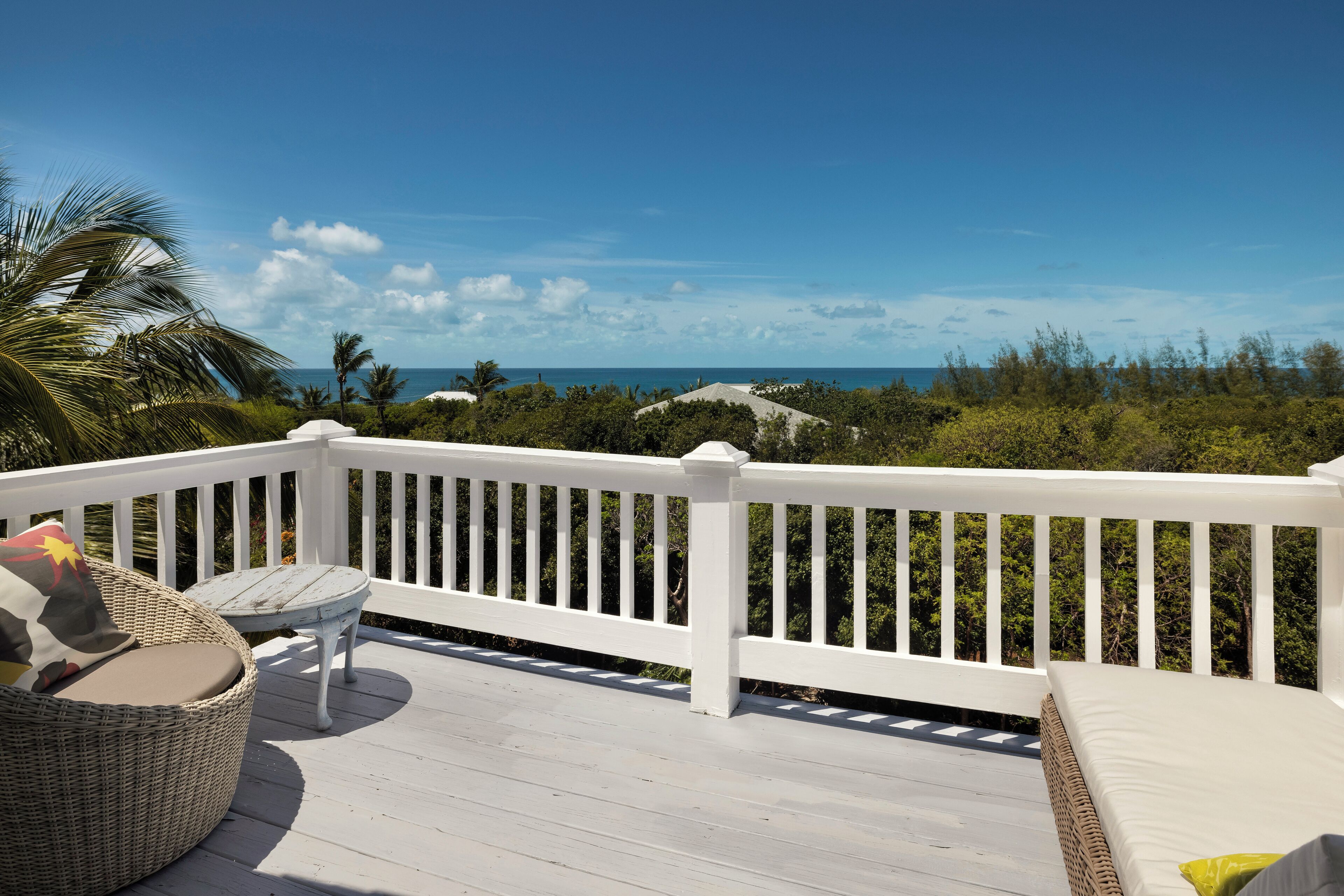 A deck with a white railing, wicker furniture, and a view of the ocean.