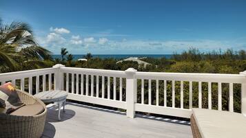 A deck with a white railing, wicker furniture, and a view of the ocean.