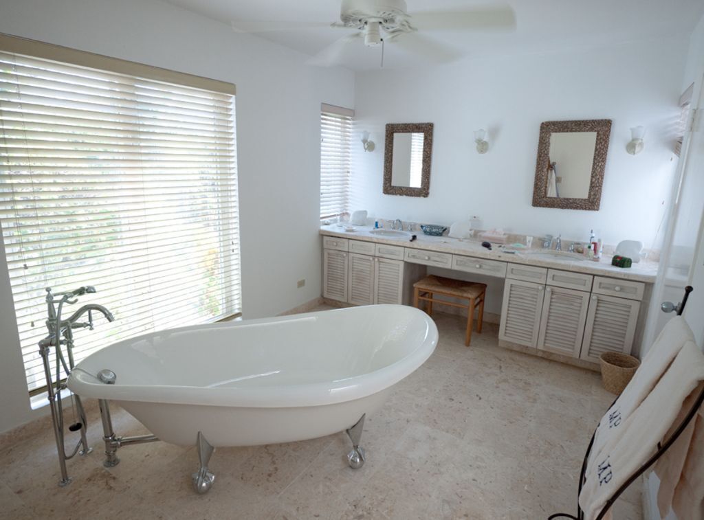 A bathroom with a freestanding bathtub, a vanity with a mirror, and a window with blinds.