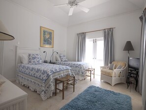 Un dormitorio con dos camas, una silla, un televisor y un ventilador de techo.