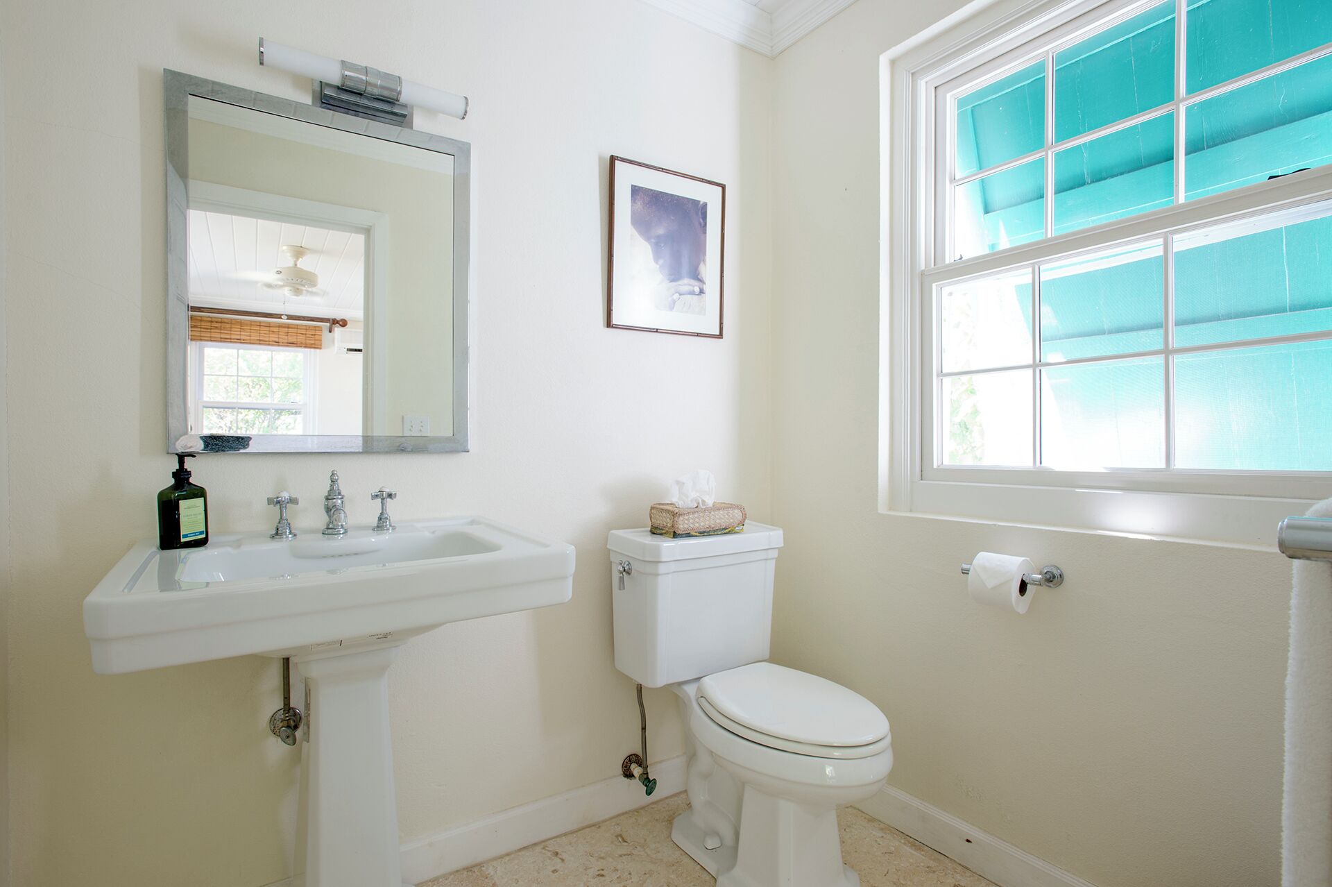 Un baño con lavamanos blanco, inodoro y ventana con vistas al exterior.