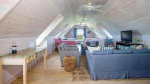 A cozy attic bedroom with a sloped ceiling, a ceiling fan, a bed, a sofa, a TV, and a small table with a lamp. - Hilltop Haven: Luxurious Historic Estate With Harbor Views (Governor's Harbour)