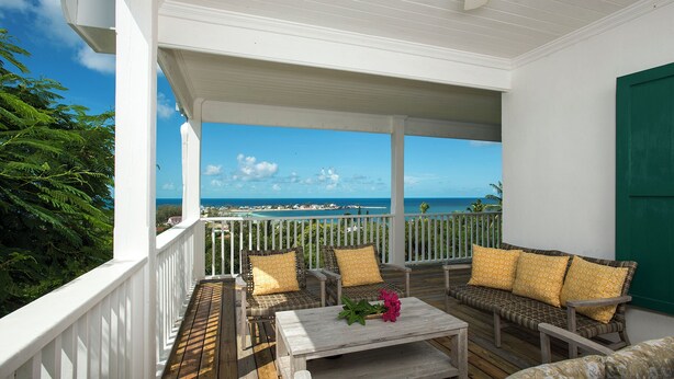 A covered outdoor seating area with wicker furniture and cushions, overlooking a coastal view. - Hilltop Haven: Luxurious Historic Estate With Harbor Views (Governor's Harbour)