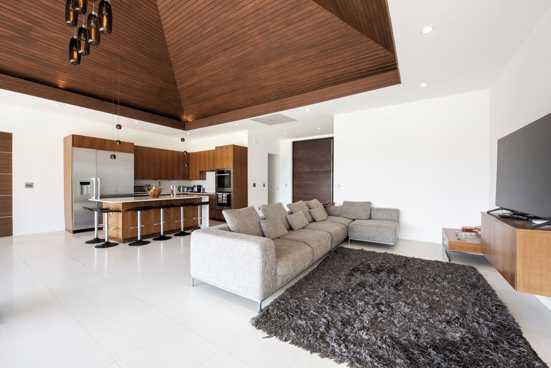 Una sala de estar moderna con un sofá modular, un televisor de pantalla plana y una zona de cocina con barra.