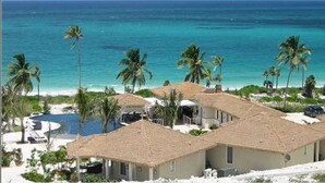 A beachfront property with thatched-roof cottages, a pool, and palm trees. - Caribbean Retreat: Private Villa With Panoramic Ocean Views (Governor's Harbour)