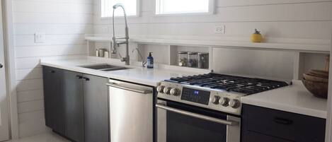 A modern kitchen with stainless steel appliances, a dishwasher, a sink, and a window above the countertop.
