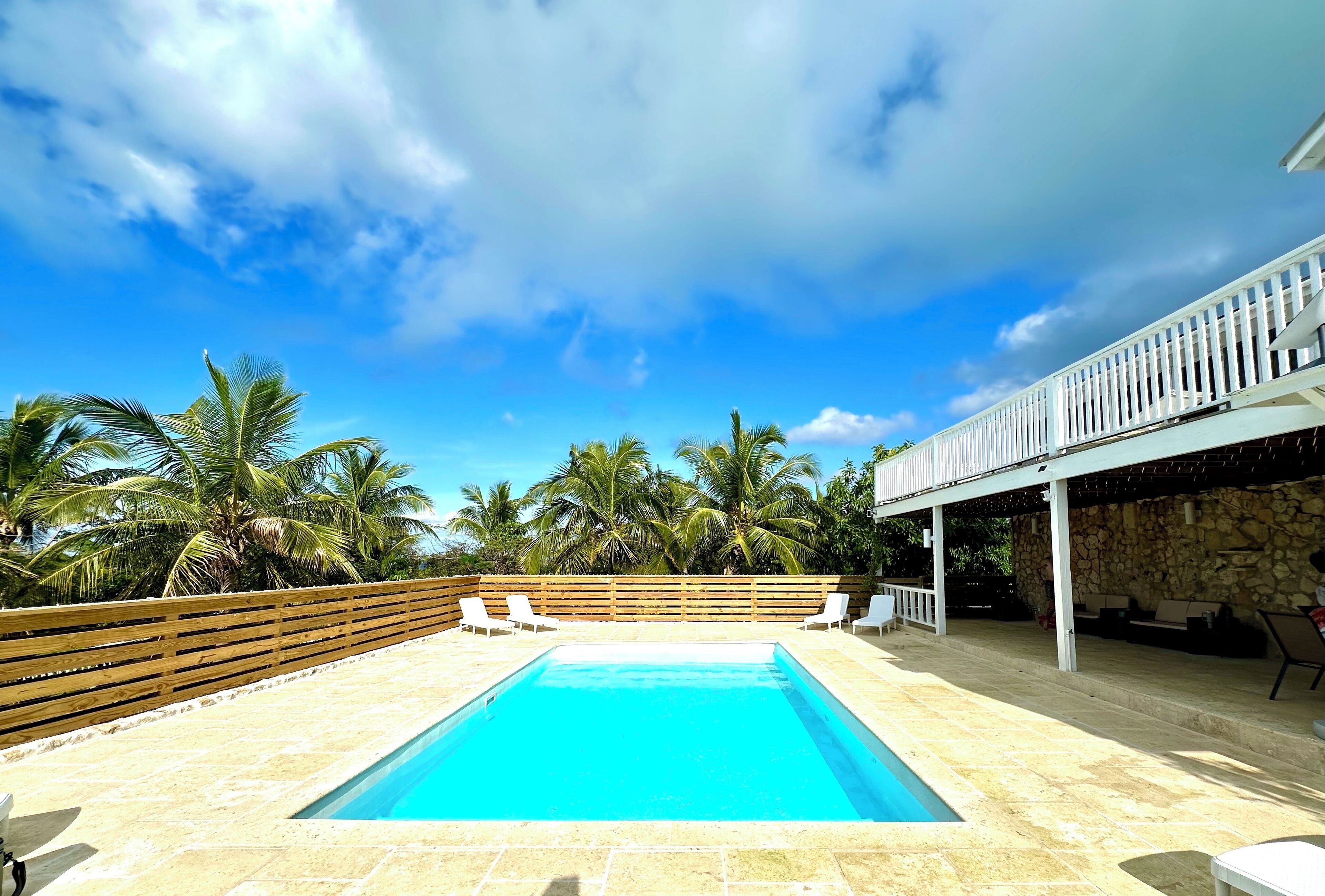 A rectangular swimming pool with a wooden deck and white lounge chairs.