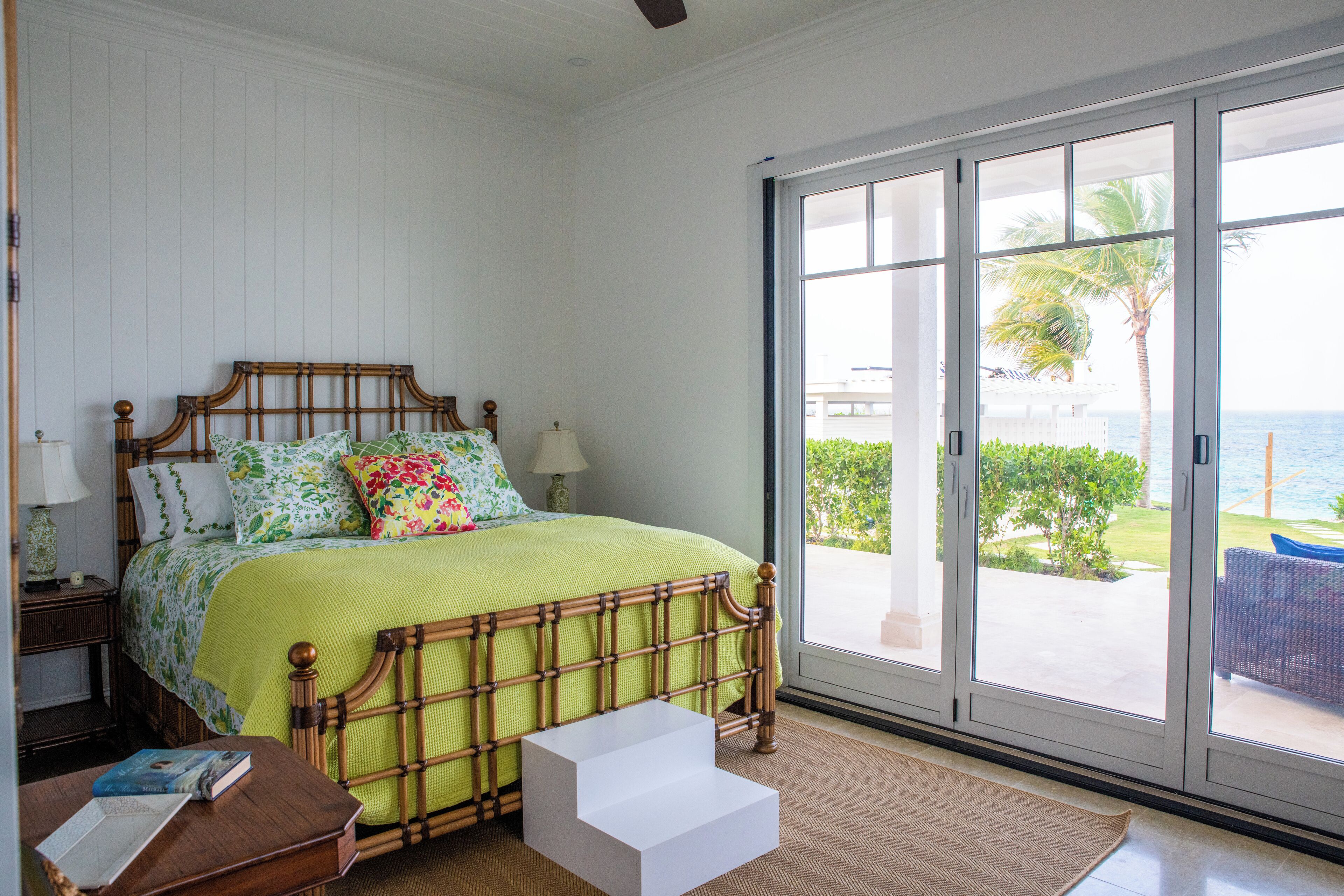 A bedroom with a bed, a nightstand, a bedside table, and a view of the outdoors through a sliding glass door.
