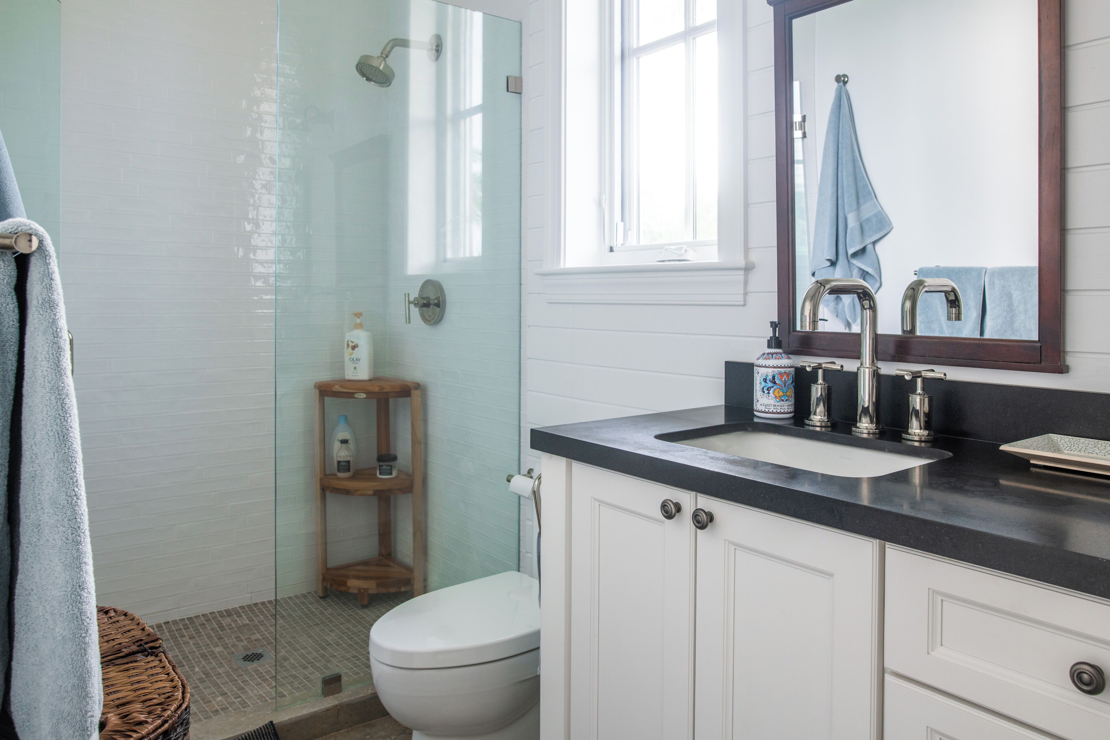 Een badkamer met een glazen douchecabine, een wit toilet, een houten plankje met toiletartikelen en een wastafel met spiegel erboven.