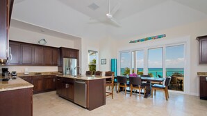 A spacious kitchen with a large island, dark wooden cabinets, and a view of the ocean through large sliding glass doors. - Coastal Luxury: New Beachfront House With Pool (North Palmetto Point)
