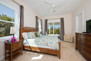 A bedroom with a large bed, a nightstand, a dresser, a television, and a view of a pool.