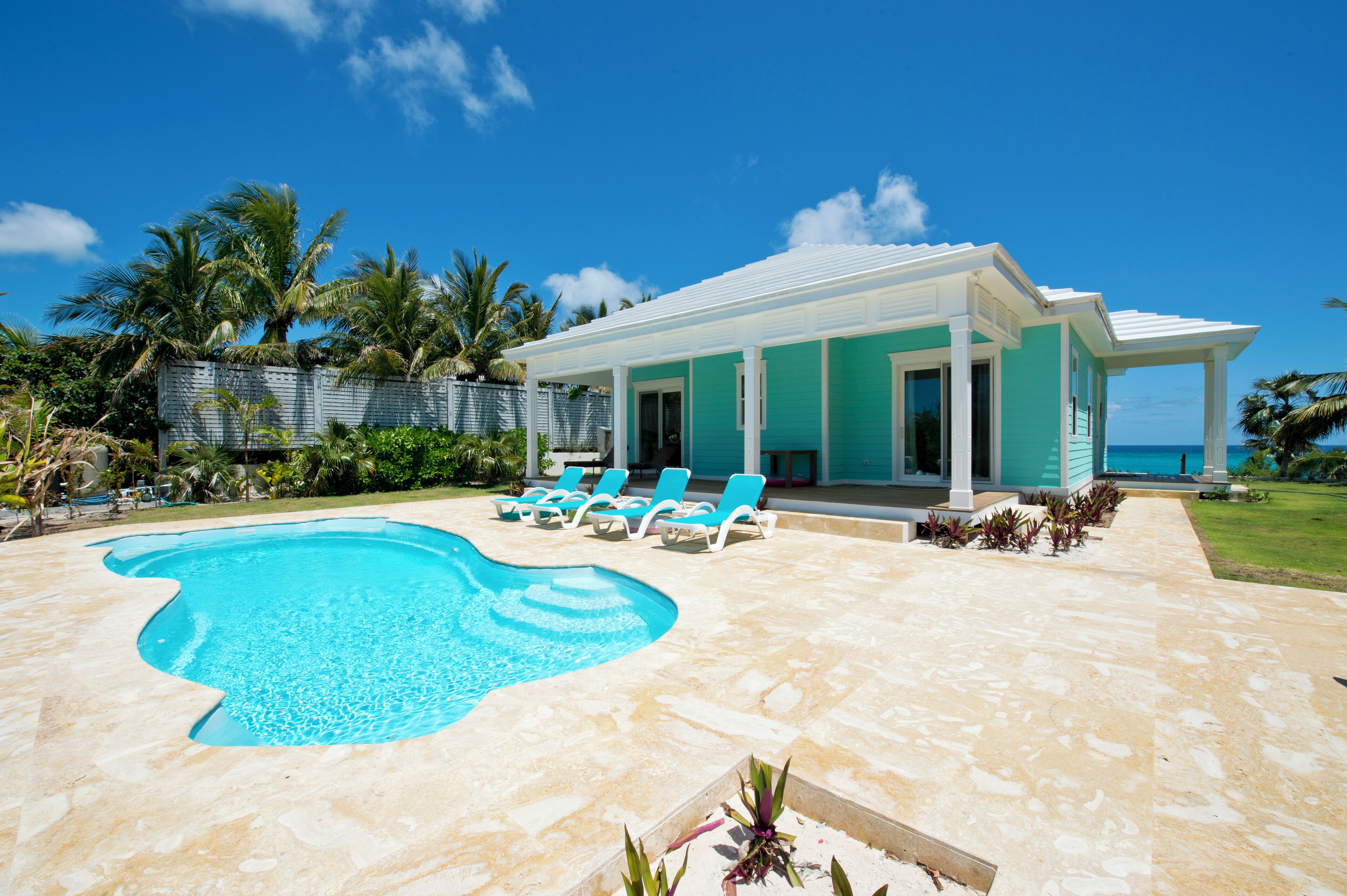 A modern house with a swimming pool, blue lounge chairs, and a view of the ocean.