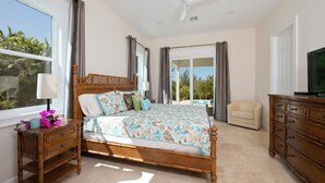 A bedroom with a large bed, a nightstand, a dresser, a television, and a view of a pool. - Buttonwood Bliss: Lux Condo With Views (James Cistern)